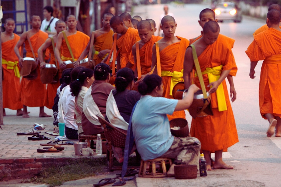 Monks in orange robes collecting alms during morning ceremony in Luang Prabang